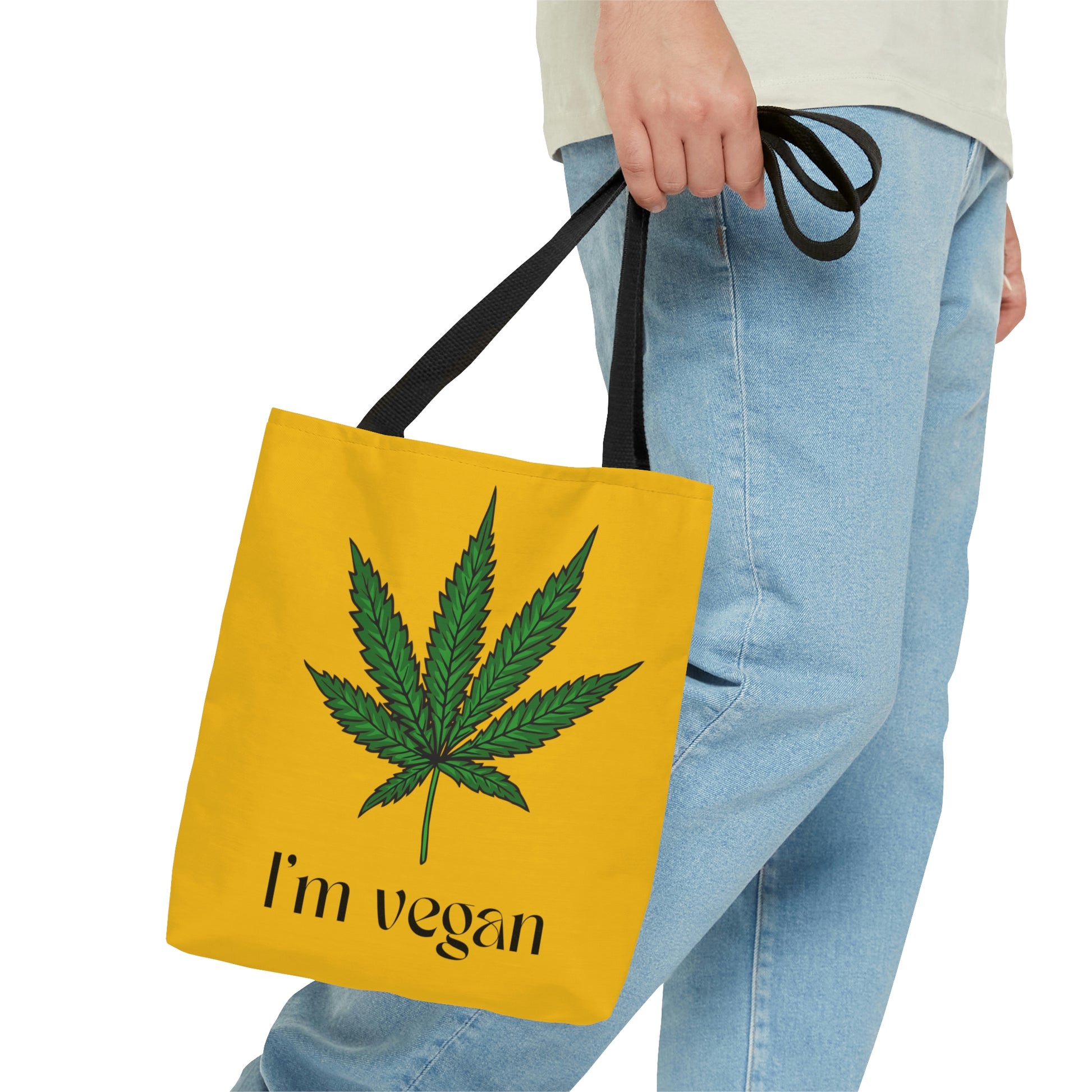 I'm Vegan Yellow Ganja Tote Bag with huge green weed leaf on front center being carried double strapped by a man in blue jeans