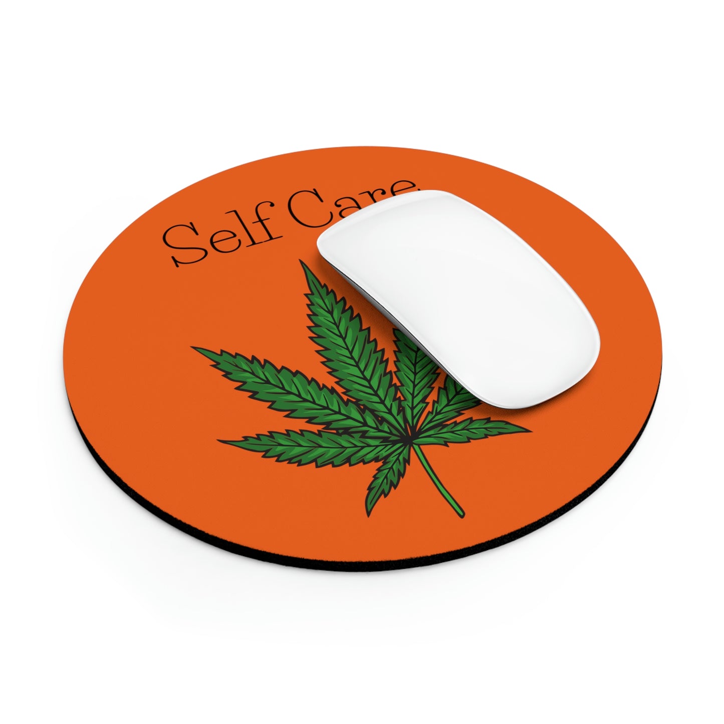 A round orange Self Care Cannabis Mouse Pad with green weed leaf on the mouse pad beneath the words self care while being complemented by a white wireless mouse.