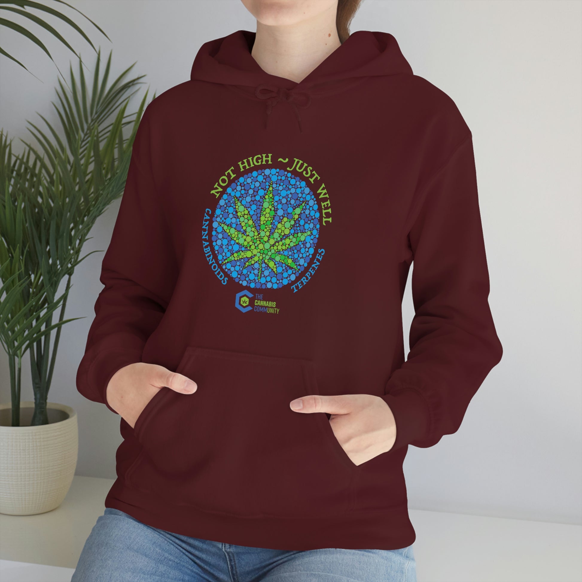 a woman wearing a maroon Not High, Just Well Cannabis Hoodie with a marijuana leaf on it.
