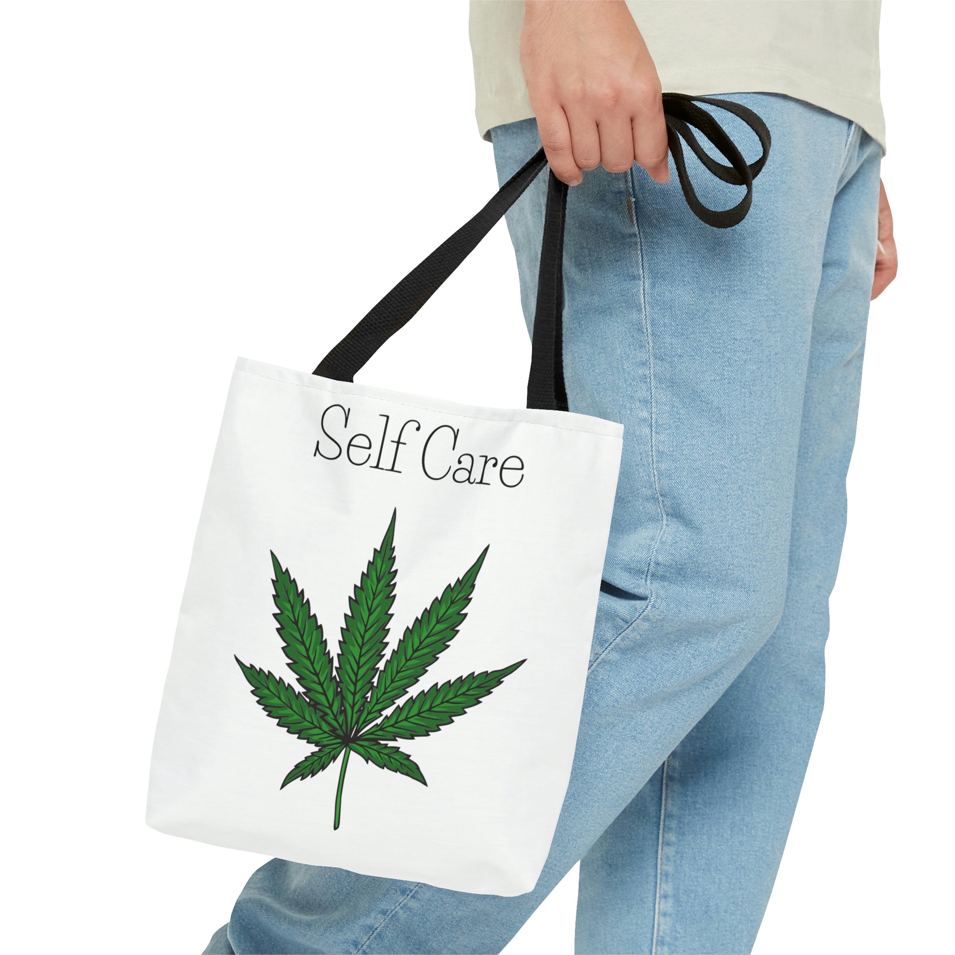A man in jeans is carrying the Self Care Cannabis Tote Bag with green marijuana leaf on front 